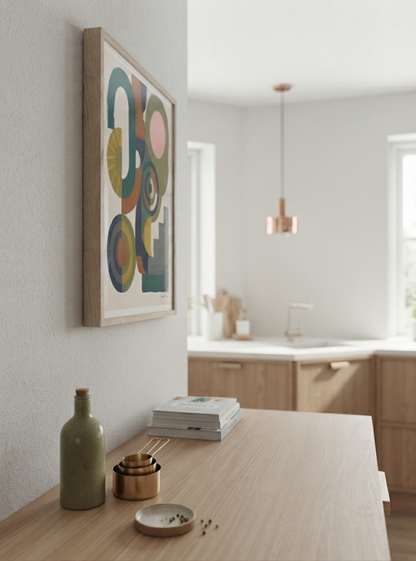 A framed Bauhaus Abstract Geometric Wall Poster with bold color block art print composition by Francis Phylae for Phylae Posters, hangs on a light gray wall above a wooden console table in a modern, softly lit kitchen or interior space. The artwork features overlapping circles and arcs in muted teal, mustard, pink, olive, and cream tones.