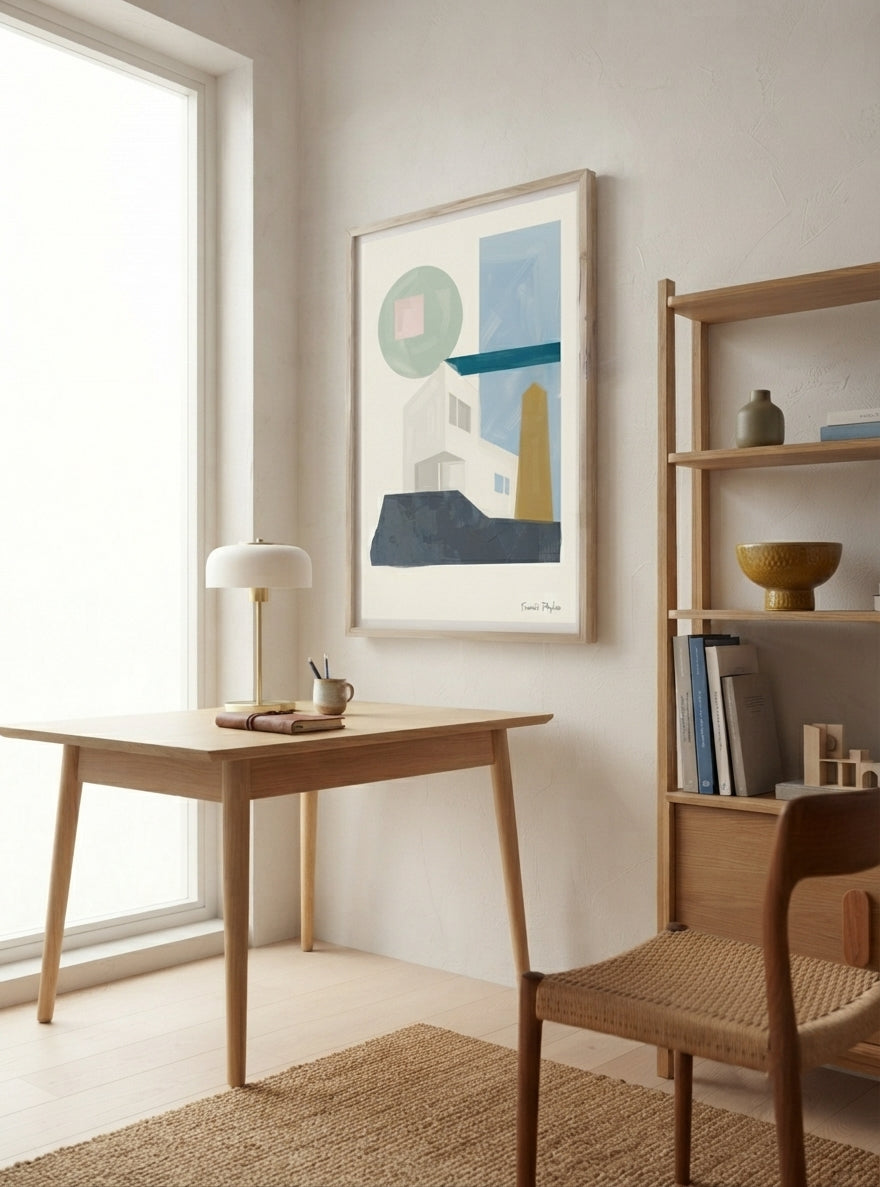 A framed abstract Bauhaus Geometric House Poster with abstract architectural design, museum-quality fine art print created from original acrylic artwork by Francis Phylae, hangs on a light beige wall in a bright, modern room. The print features shapes in blue, green, white, and yellow on a white background.