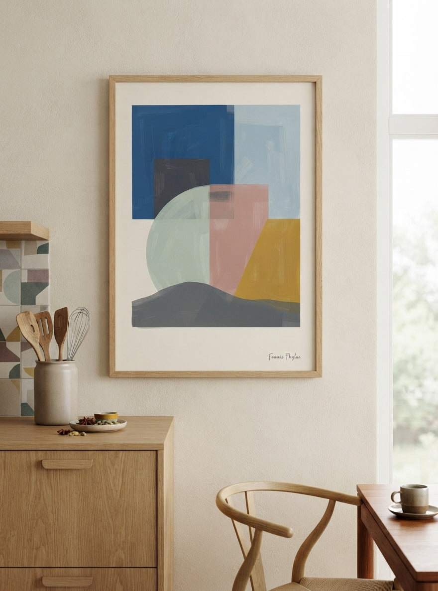 A framed Mid-Century Modern Geometric Landscape Art Print with minimalist abstract geometric print styling for living room décor by Francis Phylae at Phylae Posters, hangs on a beige wall in a modern, sunlit room. The print features blocks of blue, pink, yellow, gray, and pale green on a white background, enclosed in a light wood frame.